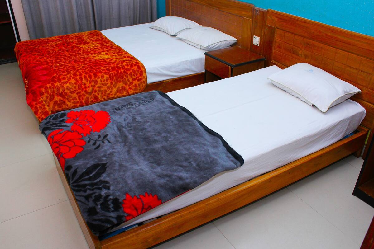 Deux lits simples avec des têtes de lit en bois, du linge de lit blanc et une couverture à motifs floraux gris sur l’un des lits.