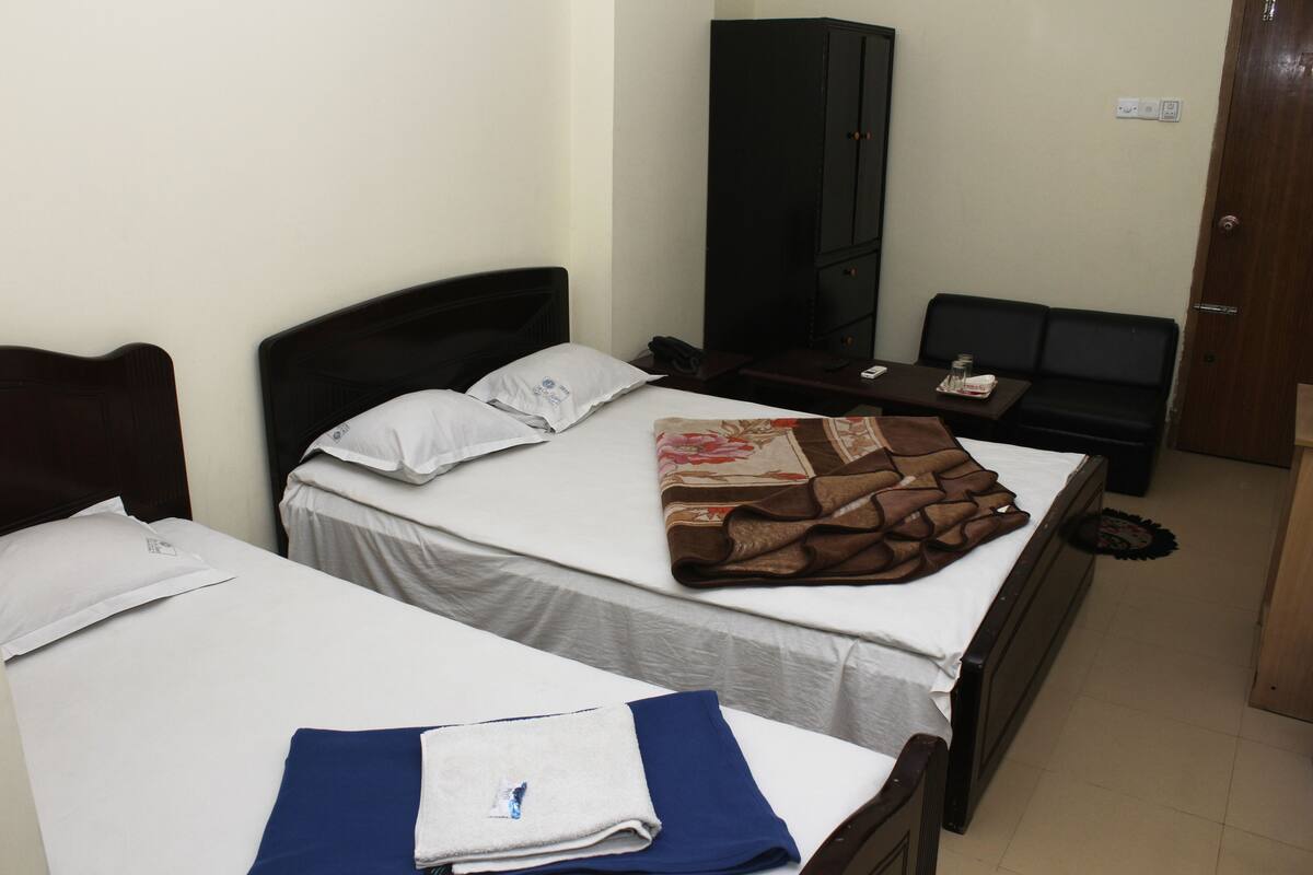 Ein Hotelzimmer mit zwei Einzelbetten, einem Kleiderschrank, einem kleinen Tisch und einem Schlafsofa.