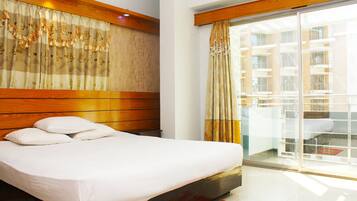 Quarto de hotel com cama, cabeceira de madeira e vista para um edifício através de uma porta de vidro.