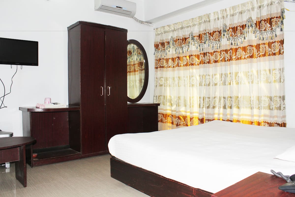Une chambre à coucher comprenant un lit, une armoire, un miroir, un téléviseur à écran plat et un rideau orné d’un motif floral.
