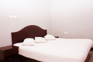 A neatly made bed with a wooden headboard, white bedding, and a bedside table. - Iqra Beach Resort (Cox's Bazar)