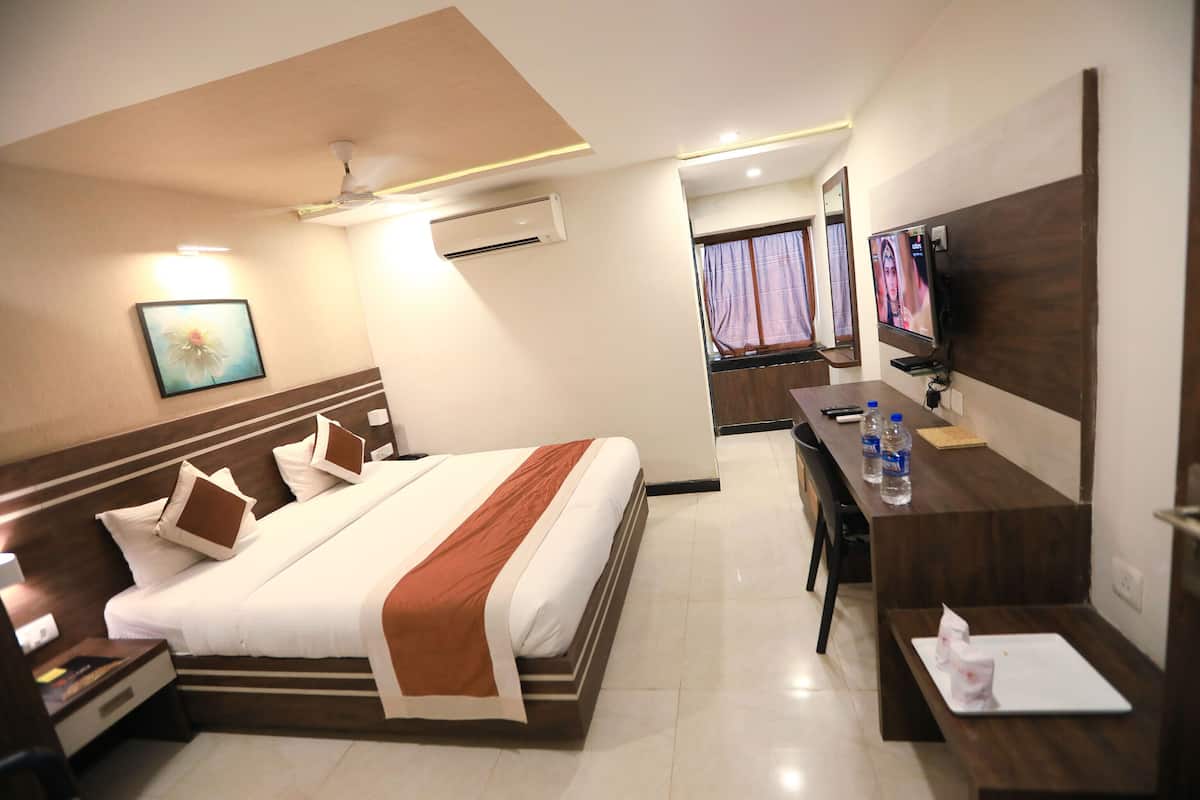 A hotel room with a bed, bedside table, desk, and a TV.