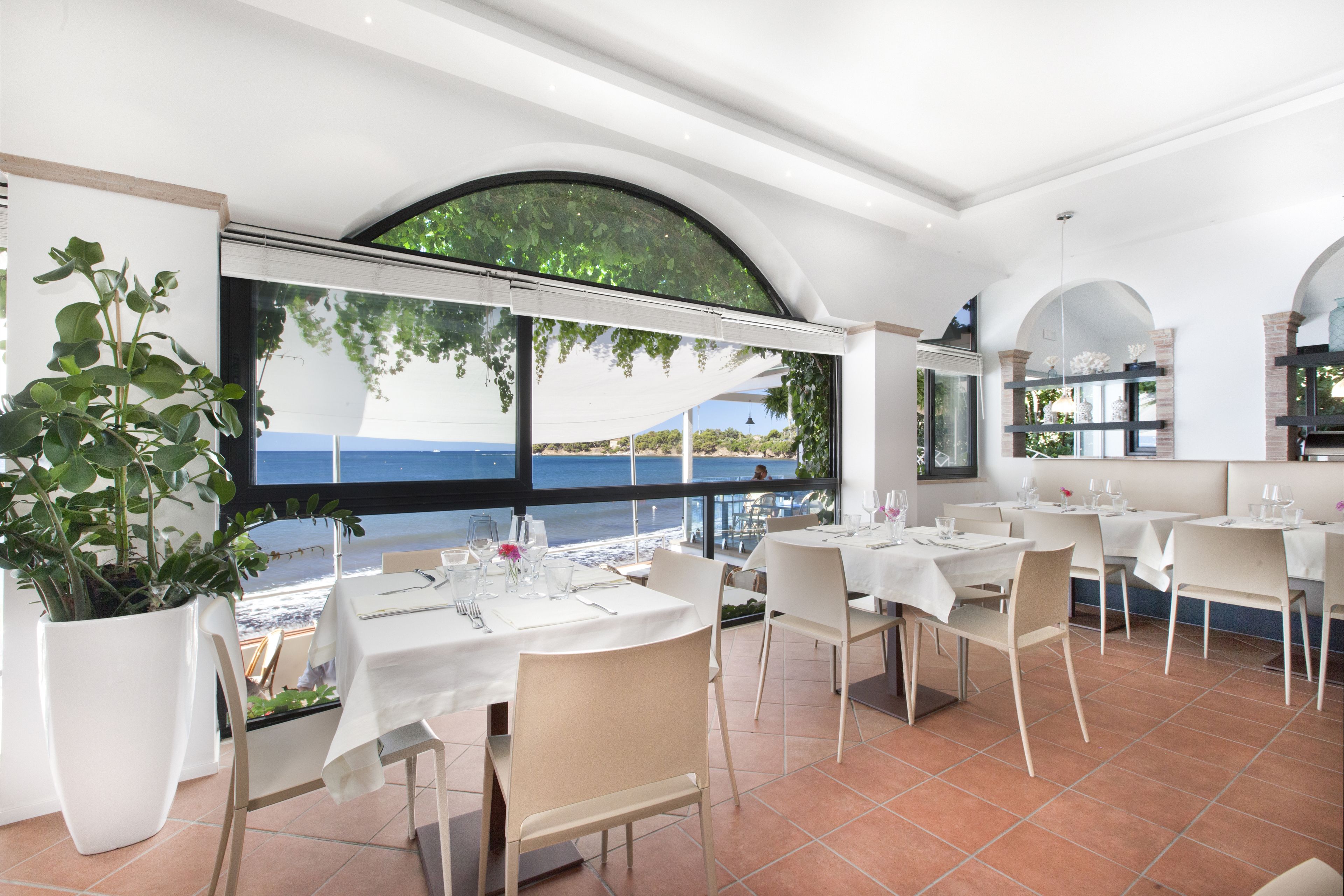 Un restaurant avec une terrasse donnant sur la plage, des tables et des chaises blanches.