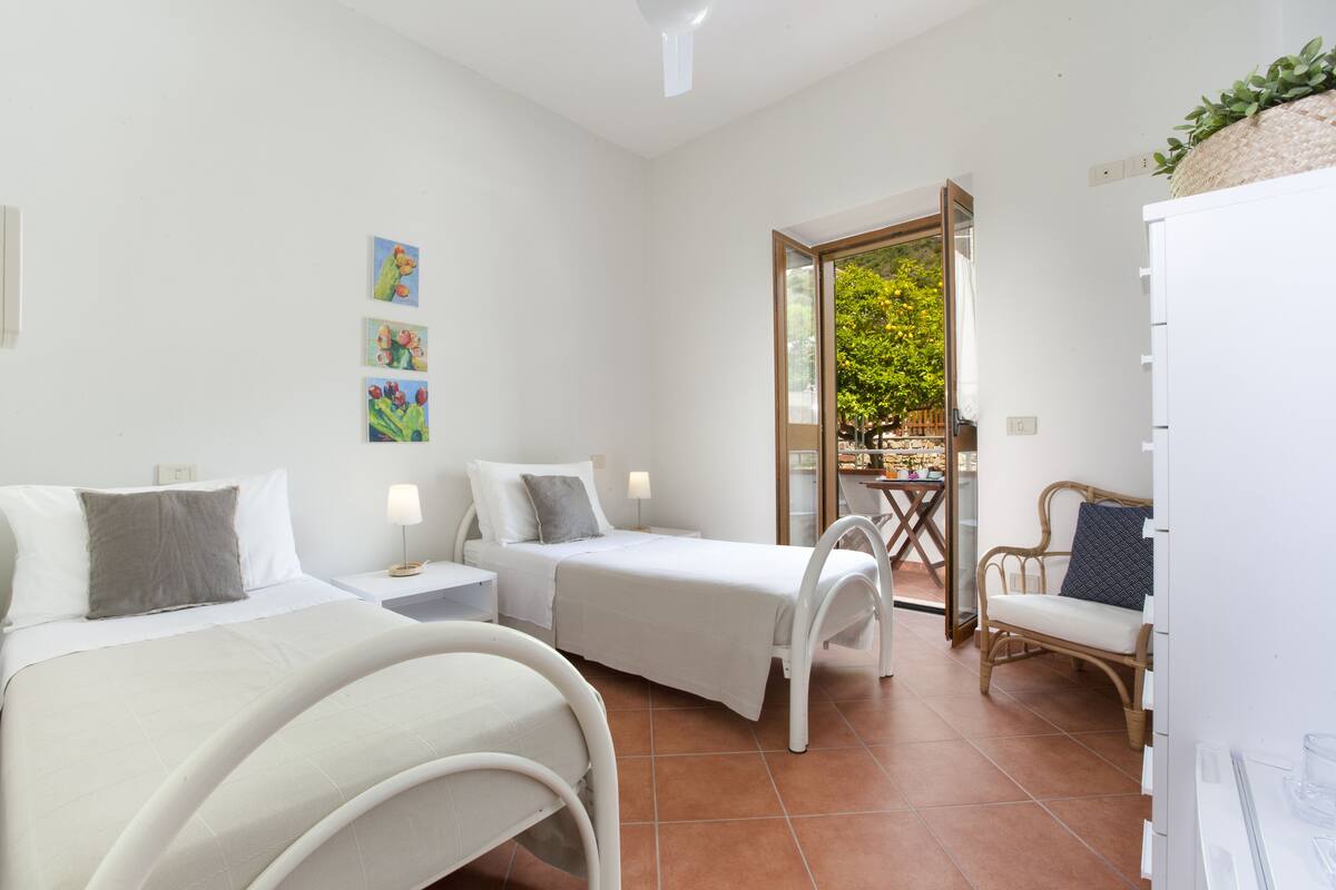 A hotel room with two beds, a small table, a chair, and a view of the outside.