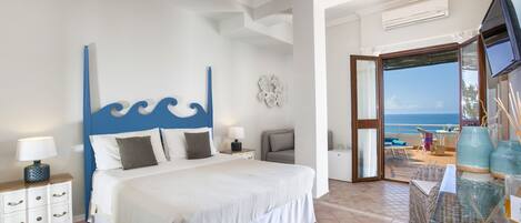 Quarto com cama, mesas de cabeceira, televisão e varanda com vista para o mar.