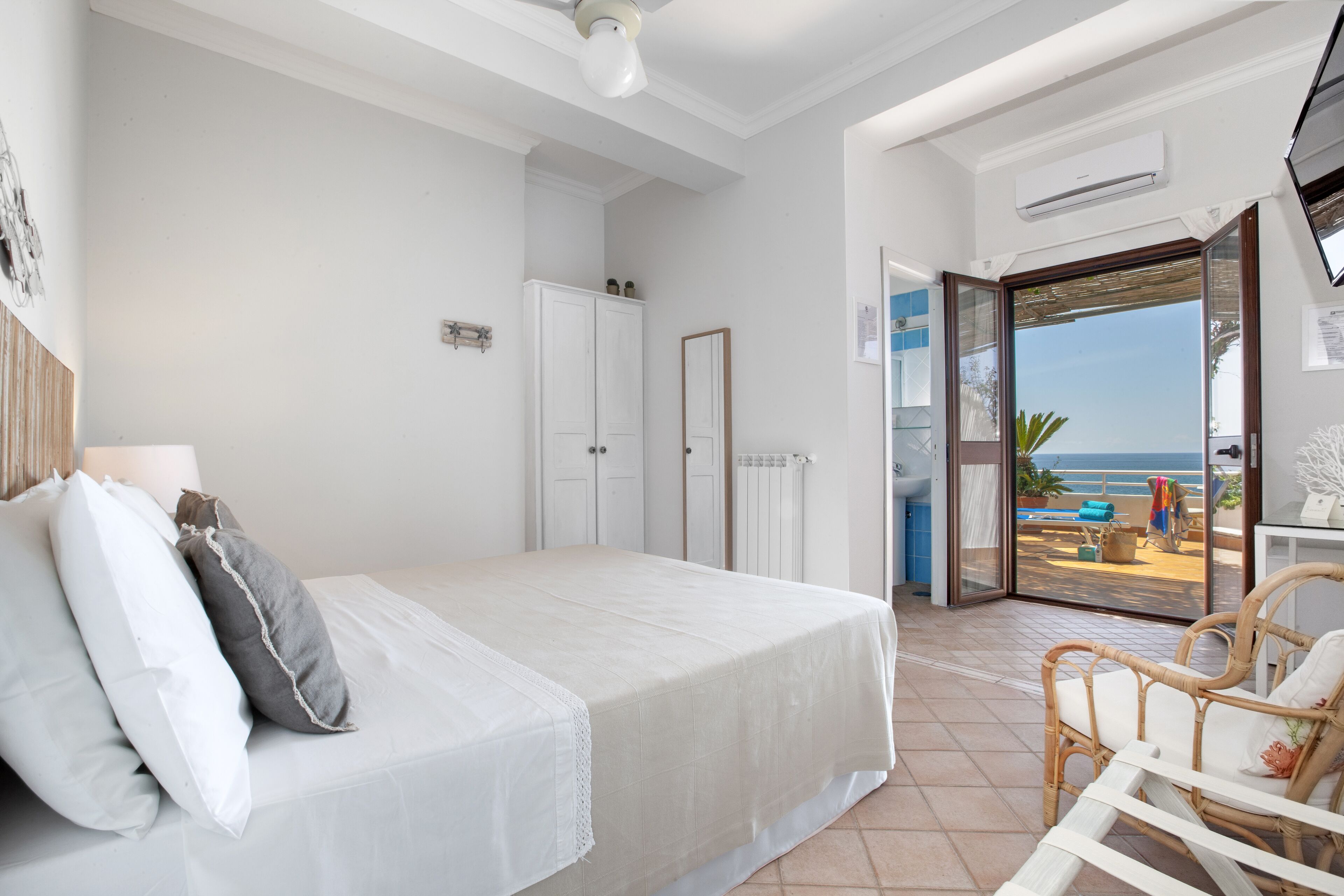 Un dormitorio con cama, una silla y vista a la playa por una puerta abierta.
