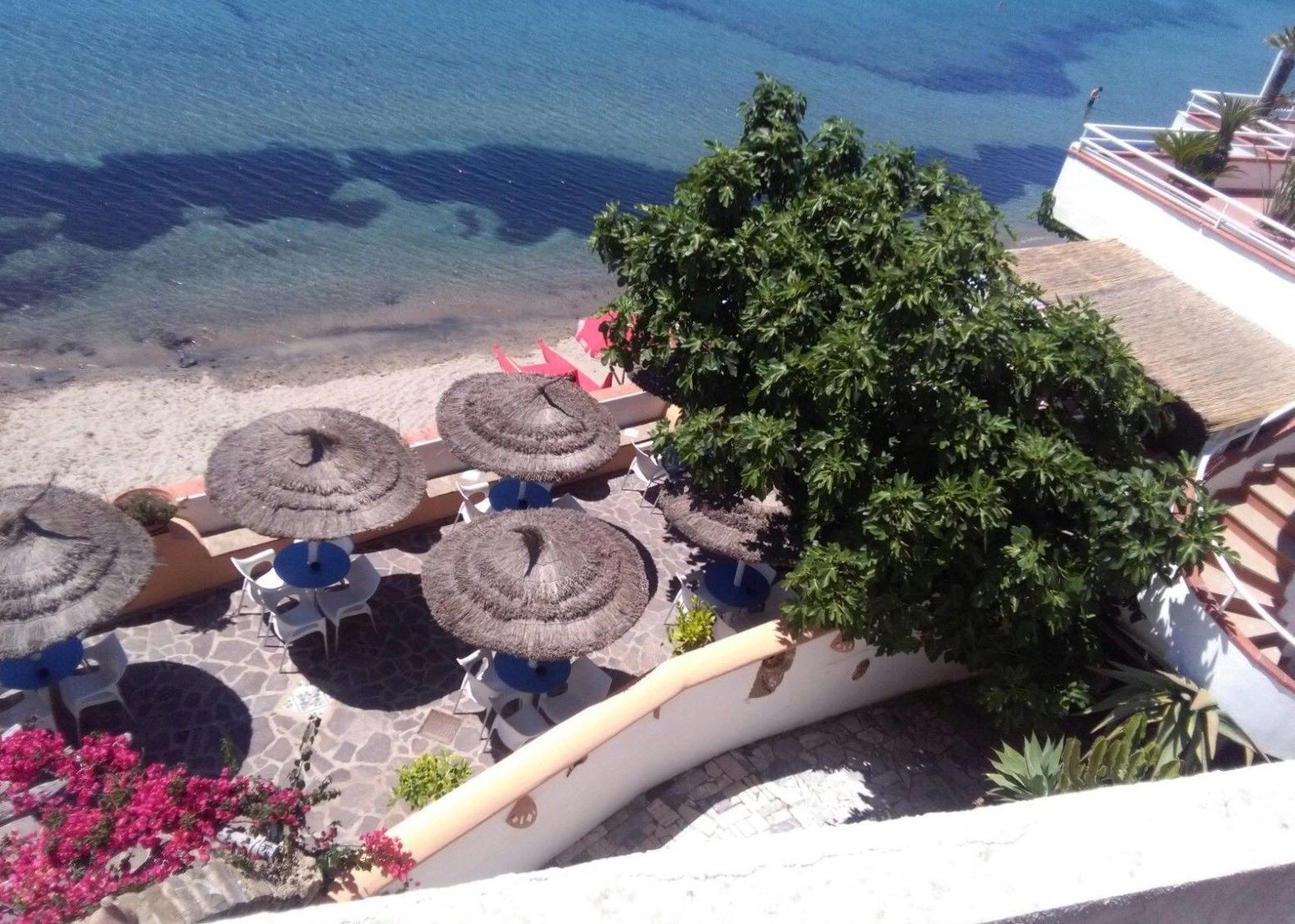 Una terraza con sombrillas de paja, mobiliario exterior y vista al mar.