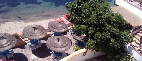 A terrace with thatched umbrellas, outdoor seating, and a view of the sea.