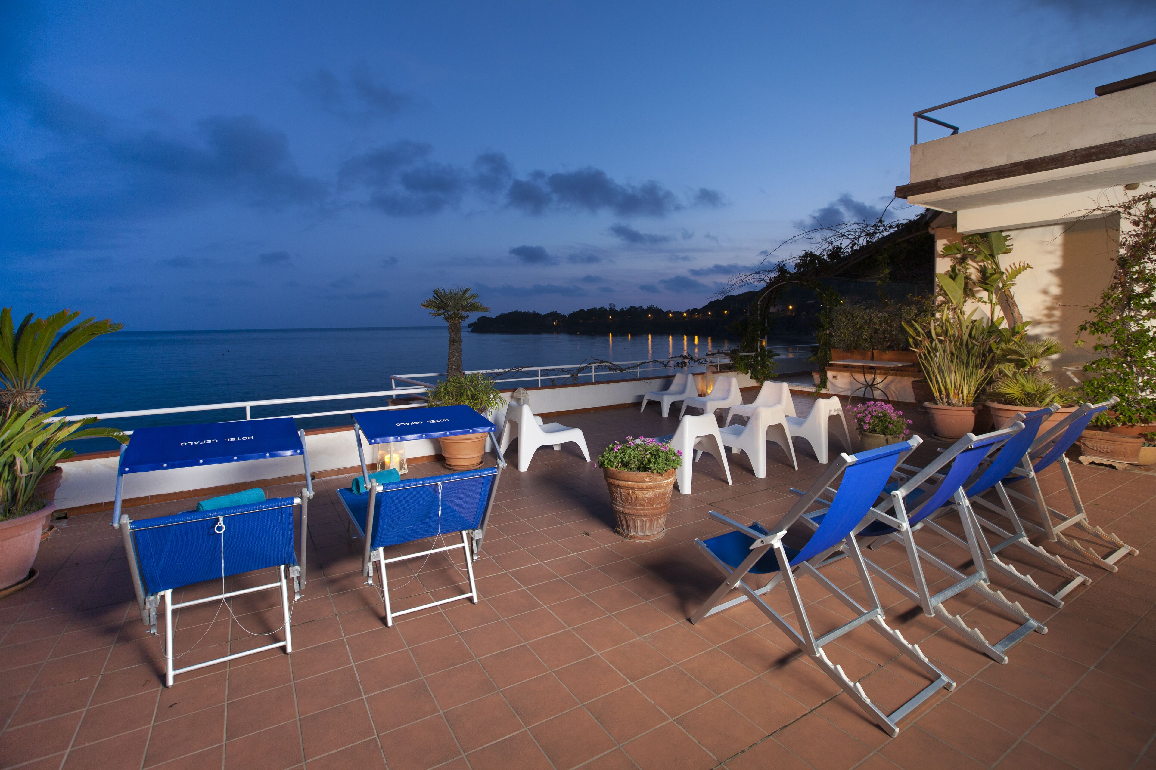 A terrace with blue lounge chairs and a table, overlooking a body of water.