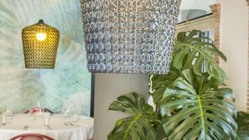 A dining area with a table set for two, a patterned hanging light fixture, and a large green plant.