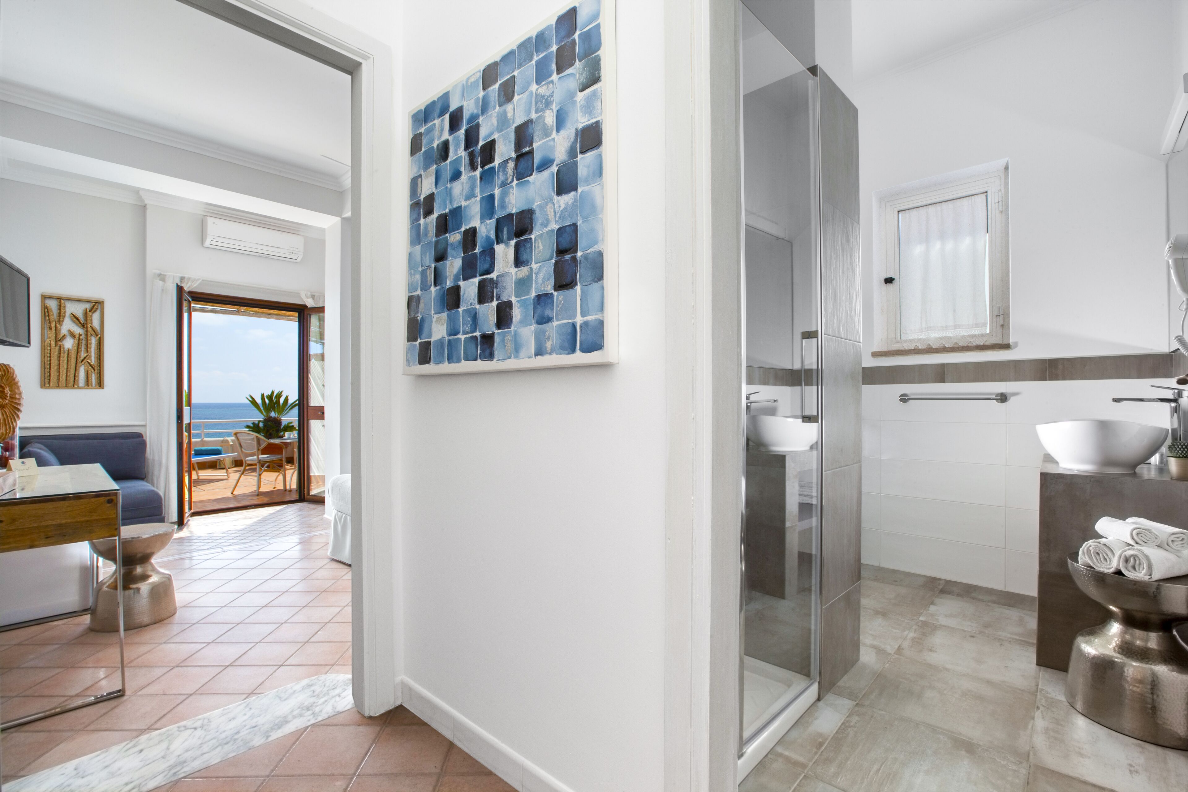 Ein modernes Badezimmer mit einer Glasdusche, einem weißen Waschbecken und Meerblick durch die geöffnete Tür.