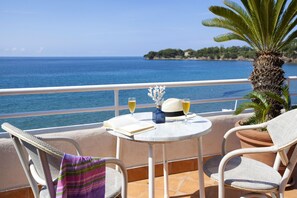 Terraço com vista para o mar, apresentando uma mesa com um livro, duas taças de vinho e um chapéu.