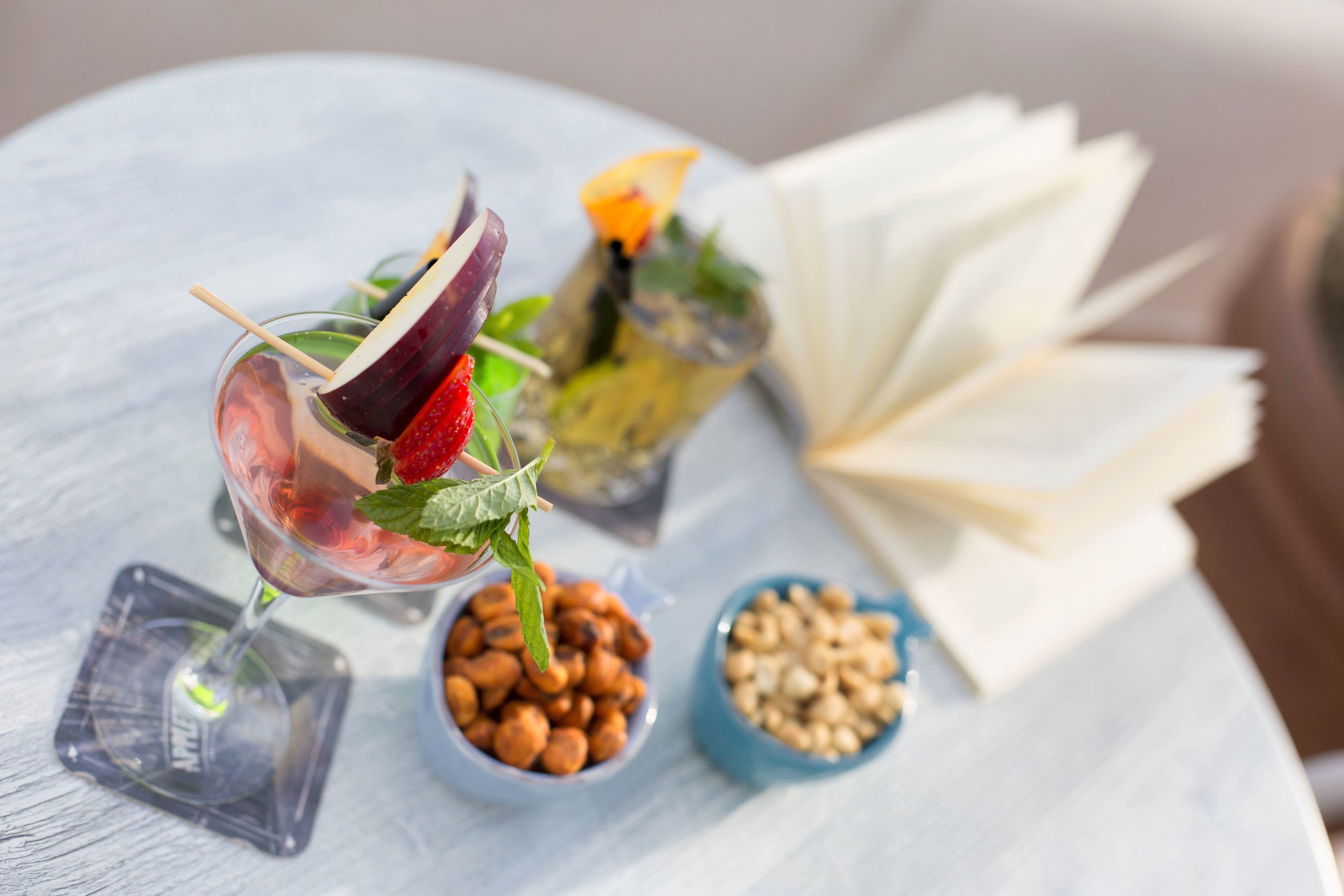 Une table avec un verre à martini, un livre et deux petits bols de noix.