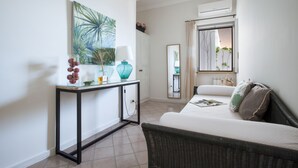 A hotel room with a bed, a wicker chair, a console table with a lamp, a mirror, and a large window with curtains. - Hotel Il Cefalo (Castellabate)