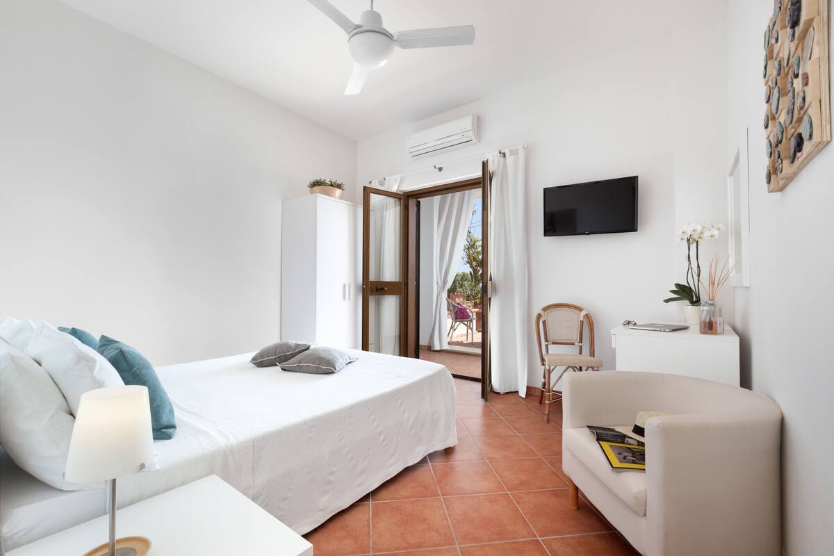 A bedroom with a bed, a chair, a TV, and an air conditioning unit.