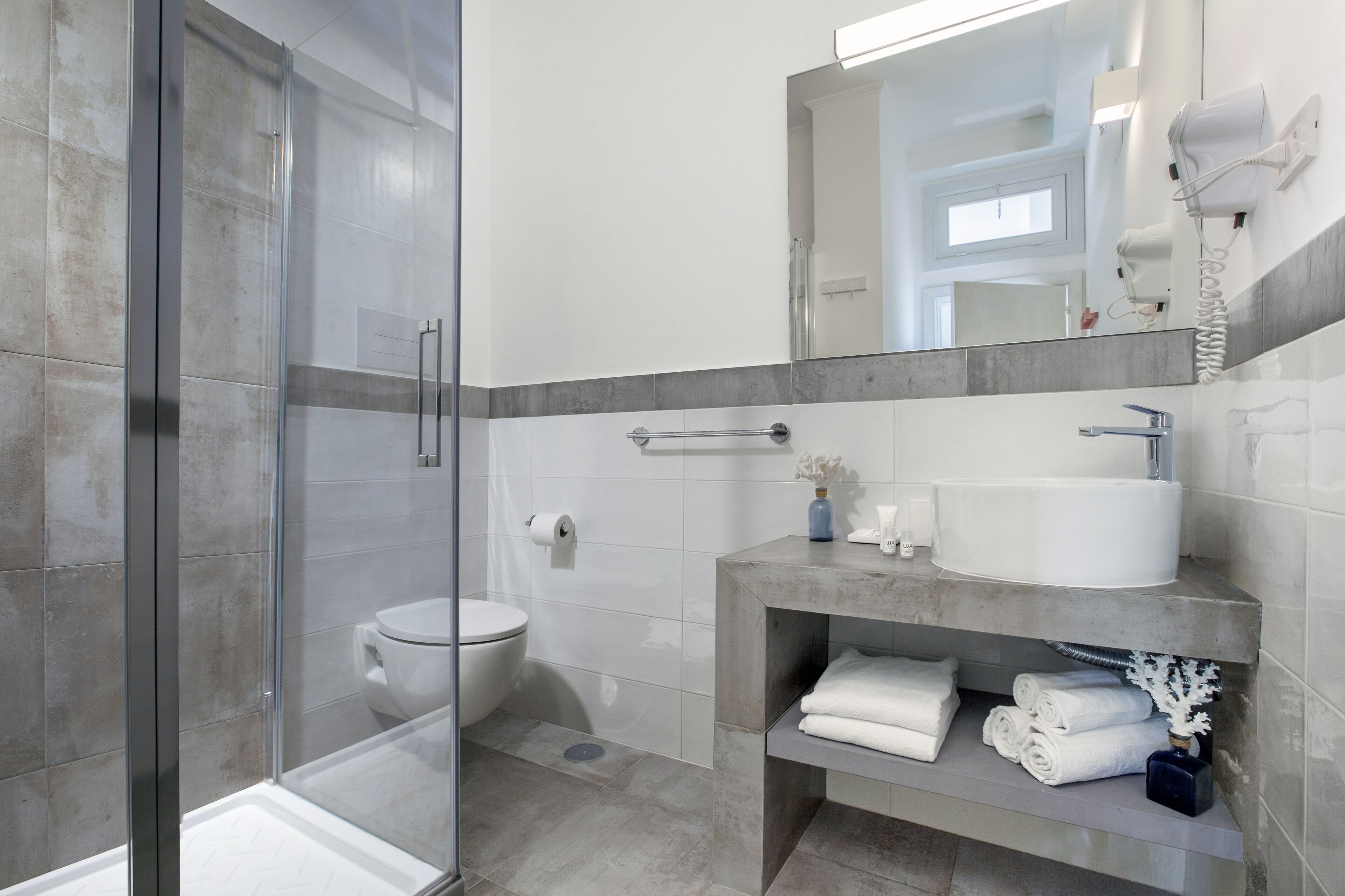 A modern bathroom with a glass shower enclosure, a toilet, a sink with a towel rack, and a mirror.