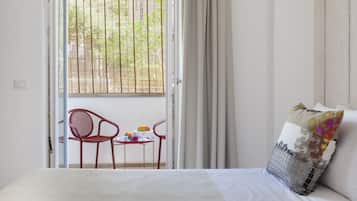 Une chambre à coucher comprenant un lit, une chaise, une petite table avec quelques objets et une fenêtre avec des stores.