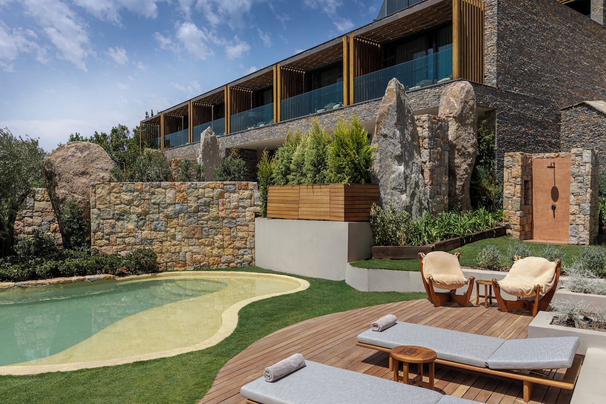 Un área de piscina moderna al aire libre con sillones reclinables y una pared de piedra.