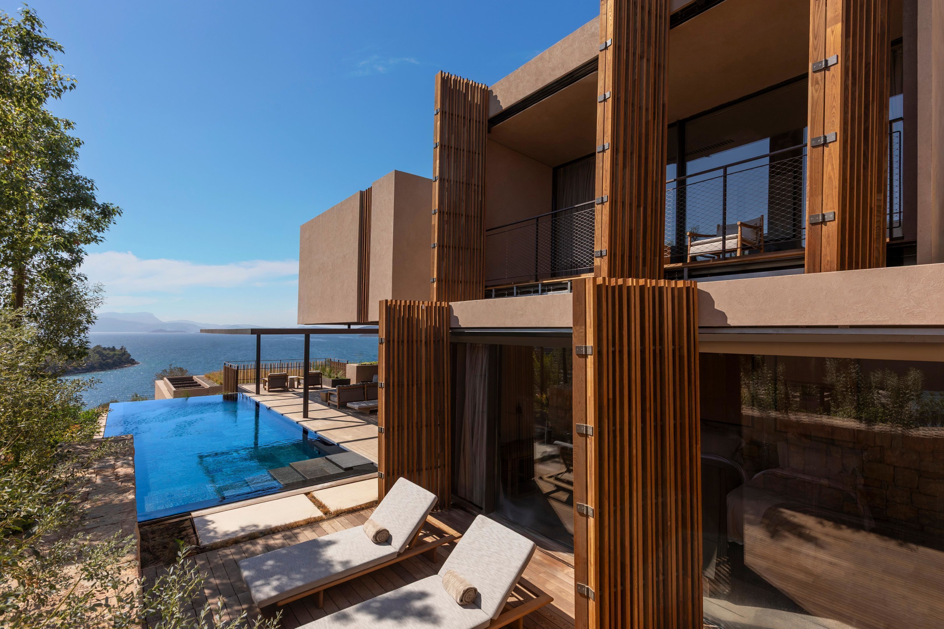 A modern building with a pool, lounge chairs, and a view of the sea.