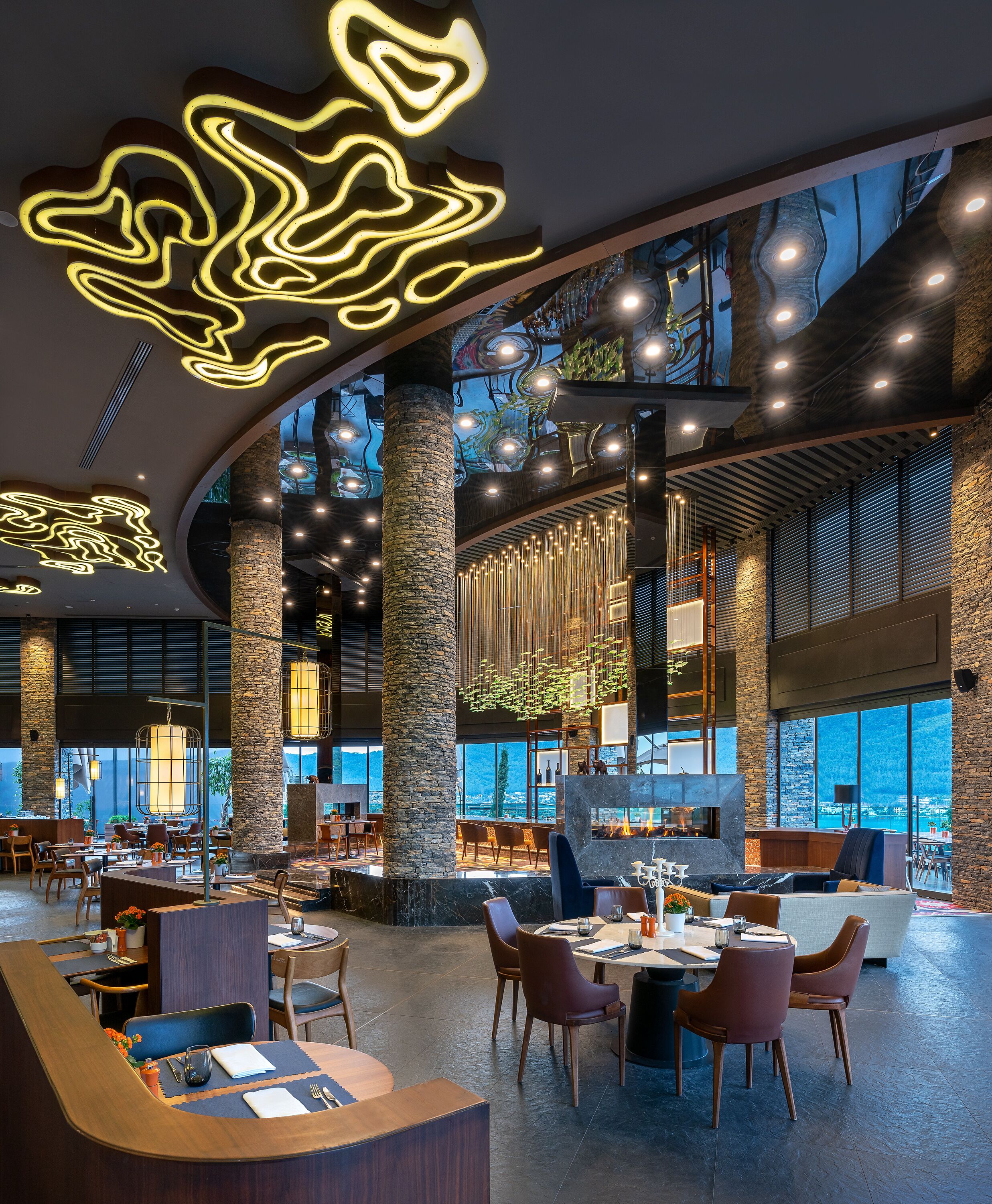 Un amplio comedor interior con techos altos, pilares de piedra e iluminación moderna.