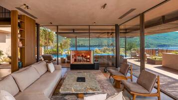 A spacious living area with a sofa, chairs, a coffee table, and a fireplace. A large window offers a view of a pool and mountains.