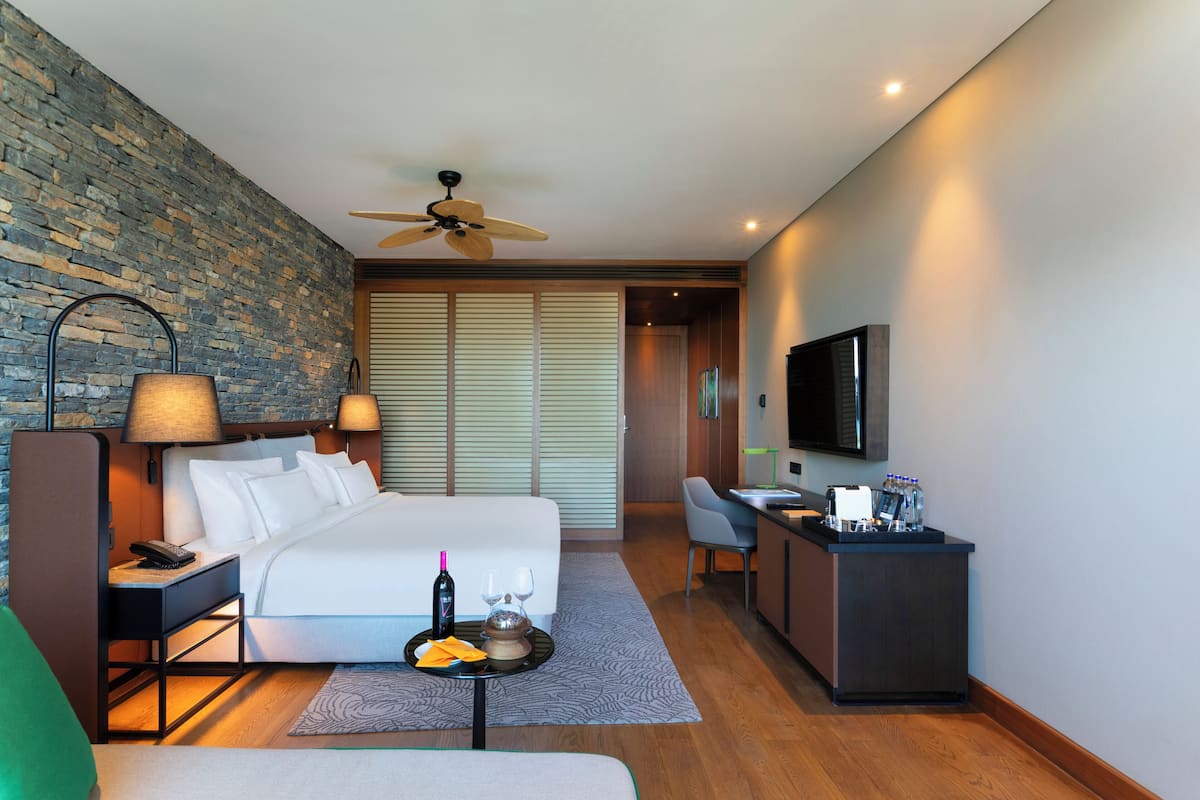 Una habitación de hotel moderna con una cama grande, un escritorio con televisor de pantalla plana, una zona de estar y una pared de acento de piedra.