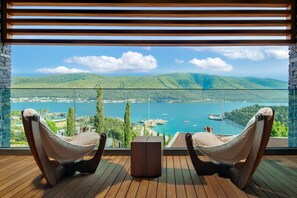 A balcony with two cushioned chairs and a small table, overlooking a lake with boats and a dock, surrounded by greenery and hills. - Lujo Hotel Bodrum (Milas)