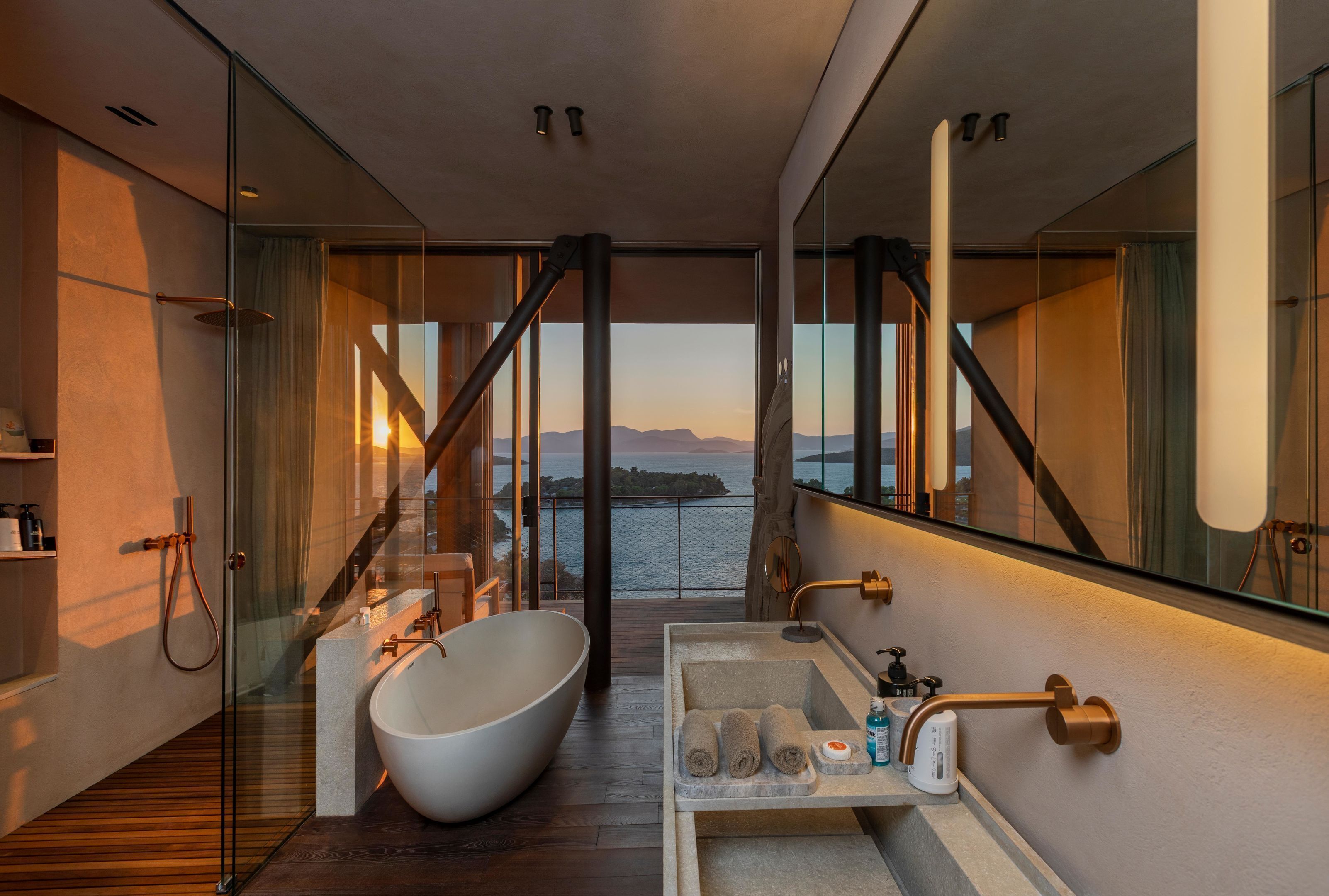 A modern bathroom with a freestanding bathtub, a glass-enclosed shower, and a view of the sea.