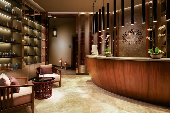 A reception area with a curved wooden reception desk, a seating area with a round wicker chair, and a shelving unit with various items.