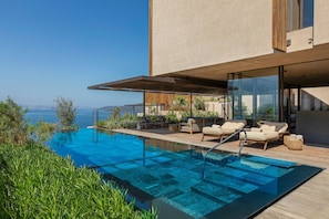 A modern pool area with a clear view of the sea, wooden deck, and lounge chairs.