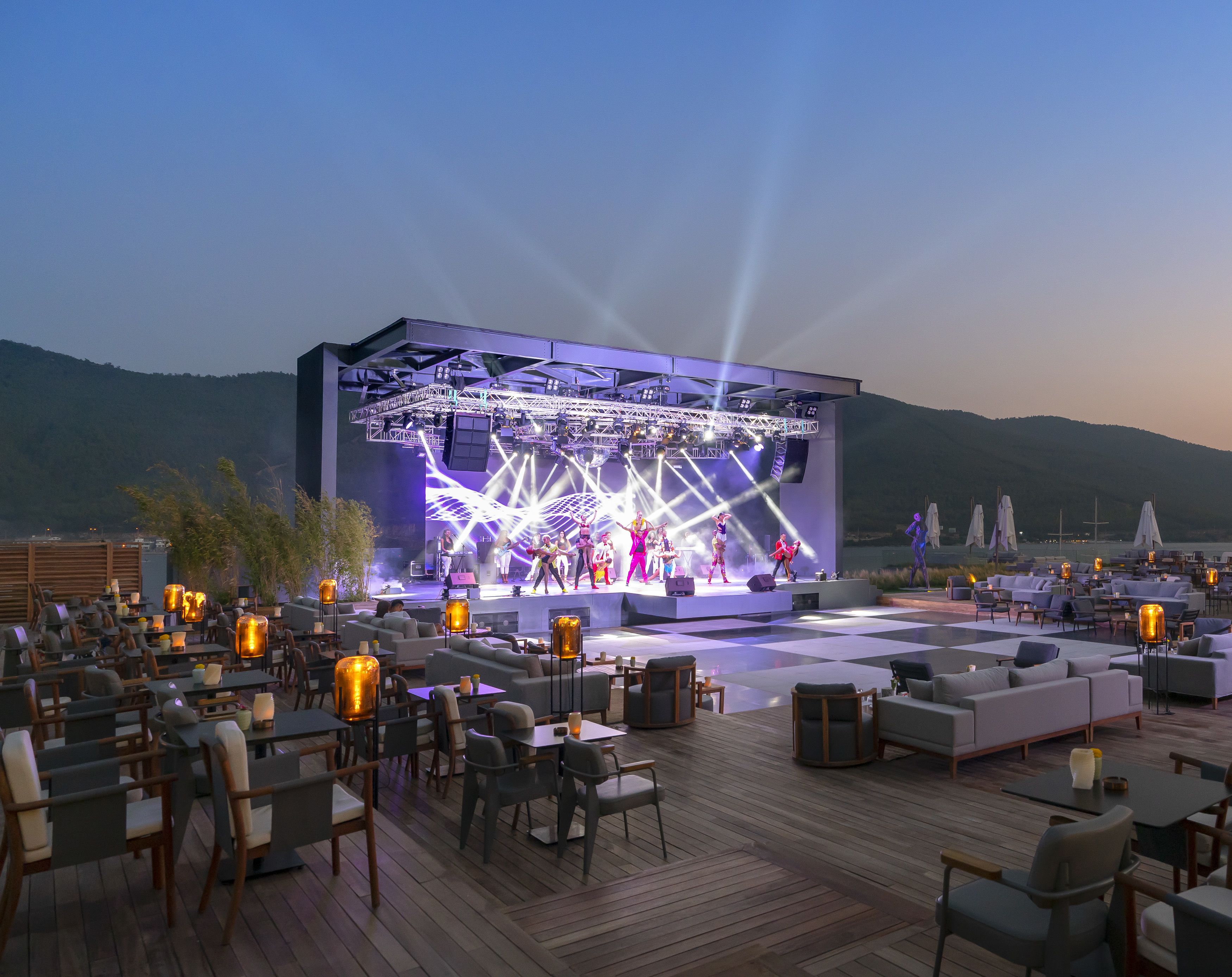 An outdoor stage with a performance, surrounded by seating areas with tables and chairs.