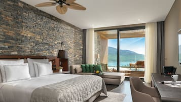 Ein modernes Hotelzimmer mit Steinwand, einem großen Bett, einer Sitzecke mit Bergblick und einem Balkon mit Tisch und Stühlen.