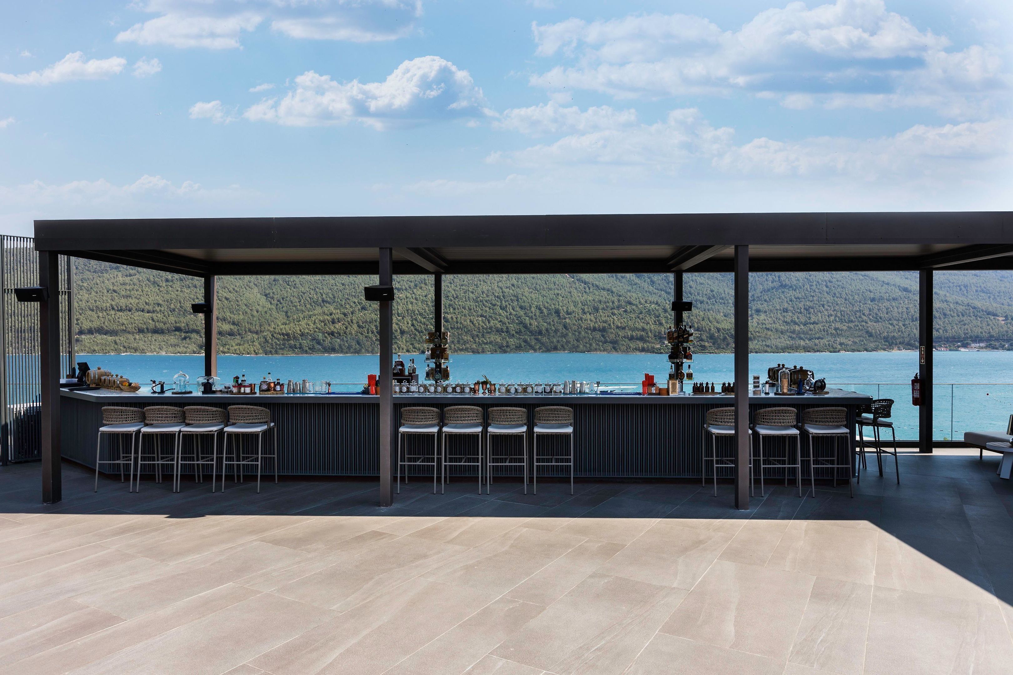 Zona de bar al aire libre cubierta con vistas a un lago y montañas.