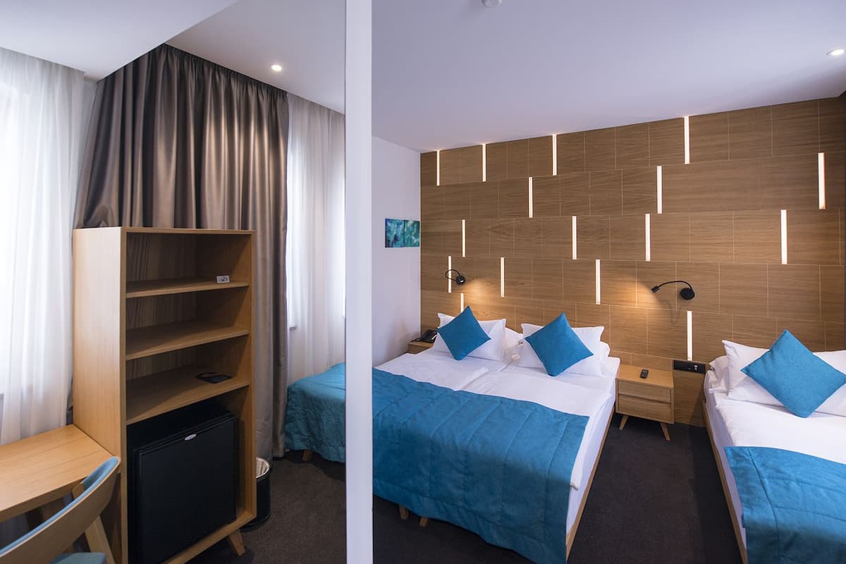 A hotel room with two beds, a desk, a wardrobe, and a small refrigerator.