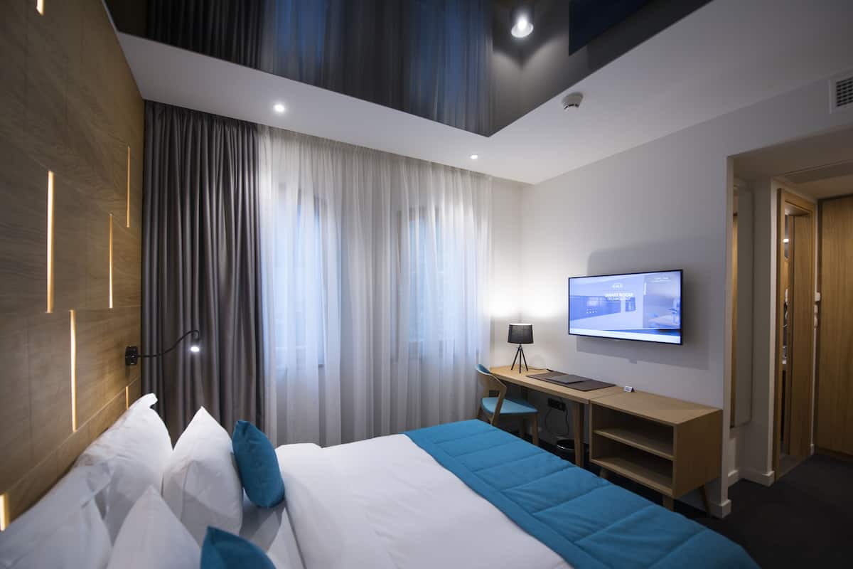 A modern hotel room with a bed, a desk, a chair, and a television.