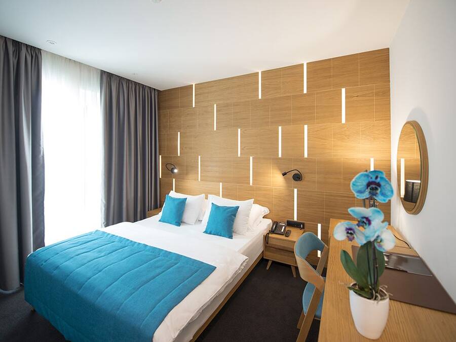 A modern hotel room with a large bed, a desk, a chair, and a potted orchid.