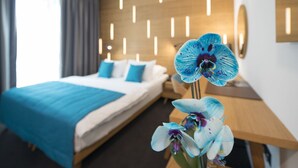A modern hotel room with a neatly made bed, a bedside table with a vase of flowers, and a wall-mounted light fixture. - Hotel Sana (Sarajevo)