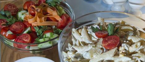 A buffet table with various dishes including a salad, pasta, and a bowl of olives.