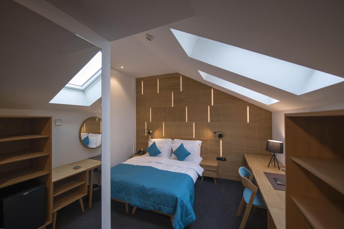 A modern bedroom with a skylight, a bed with blue bedding, a desk, and a chair.
