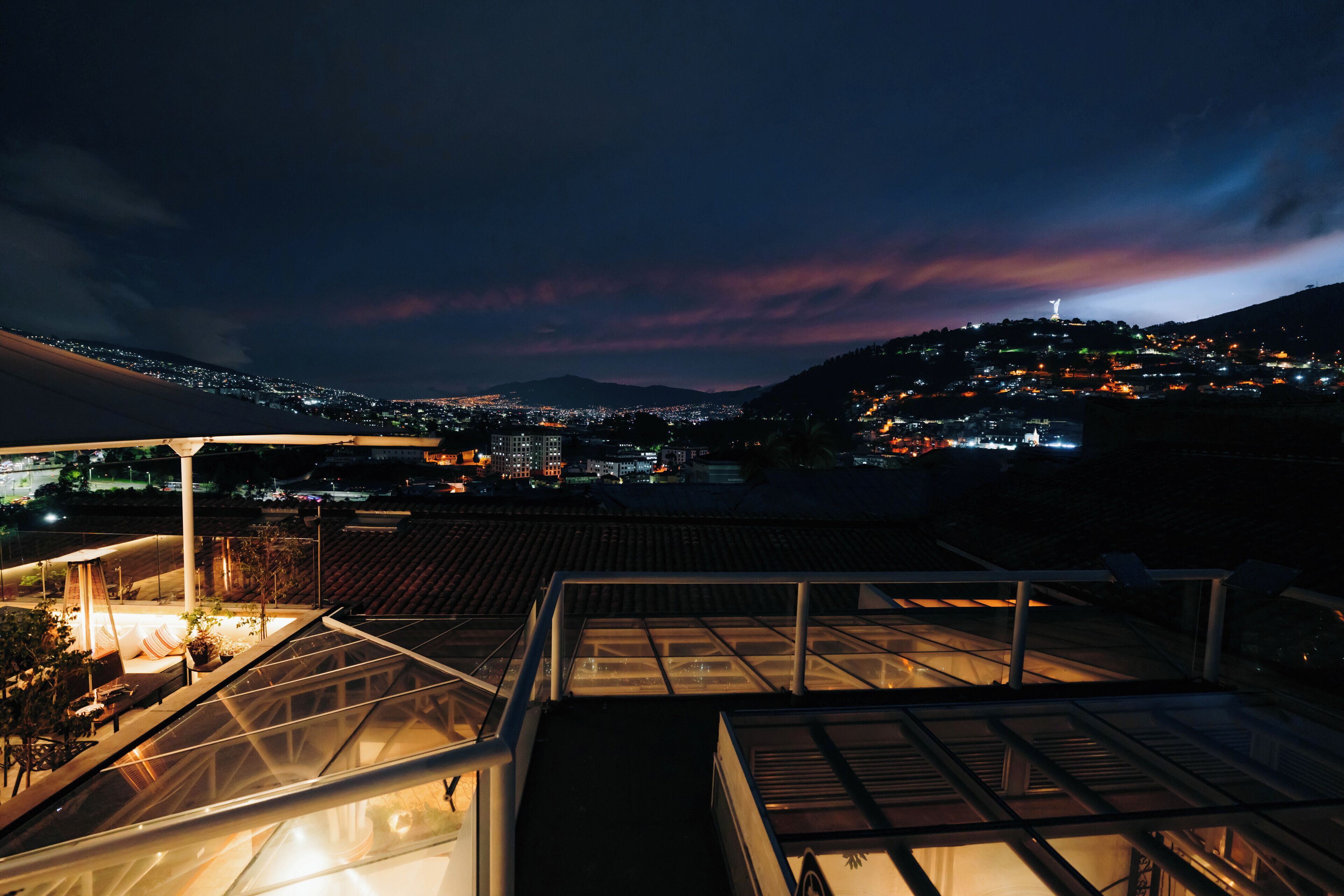 Terraza en la azotea con cerramiento de vidrio, con vistas a un paisaje urbano nocturno.