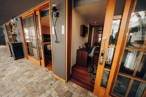 Entrada de hotel con puerta de vidrio, escalera de madera y un interior visible que incluye una cama y un baño.