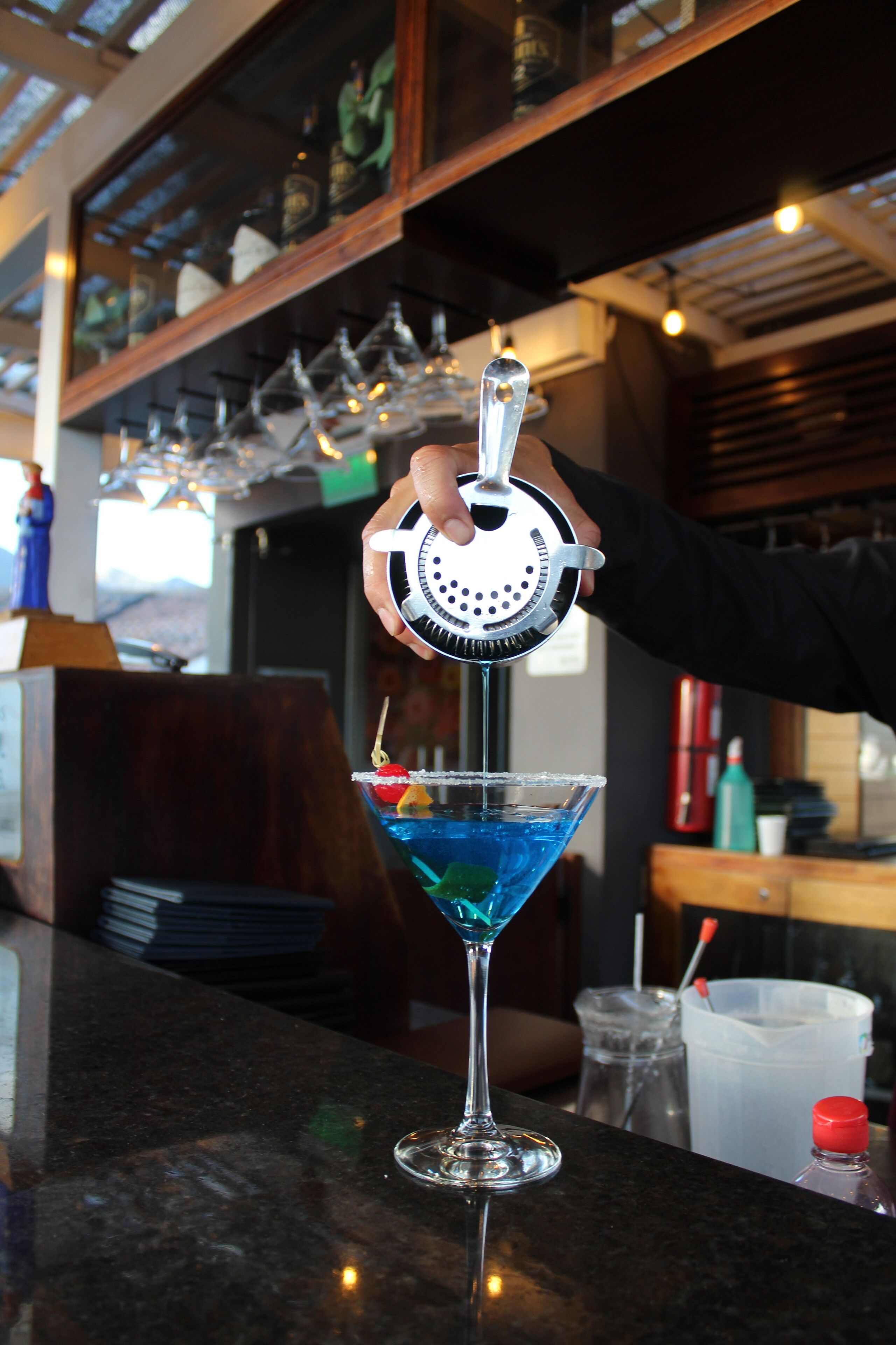 Un bartender sirviendo un cóctel azul en una copa de martini.