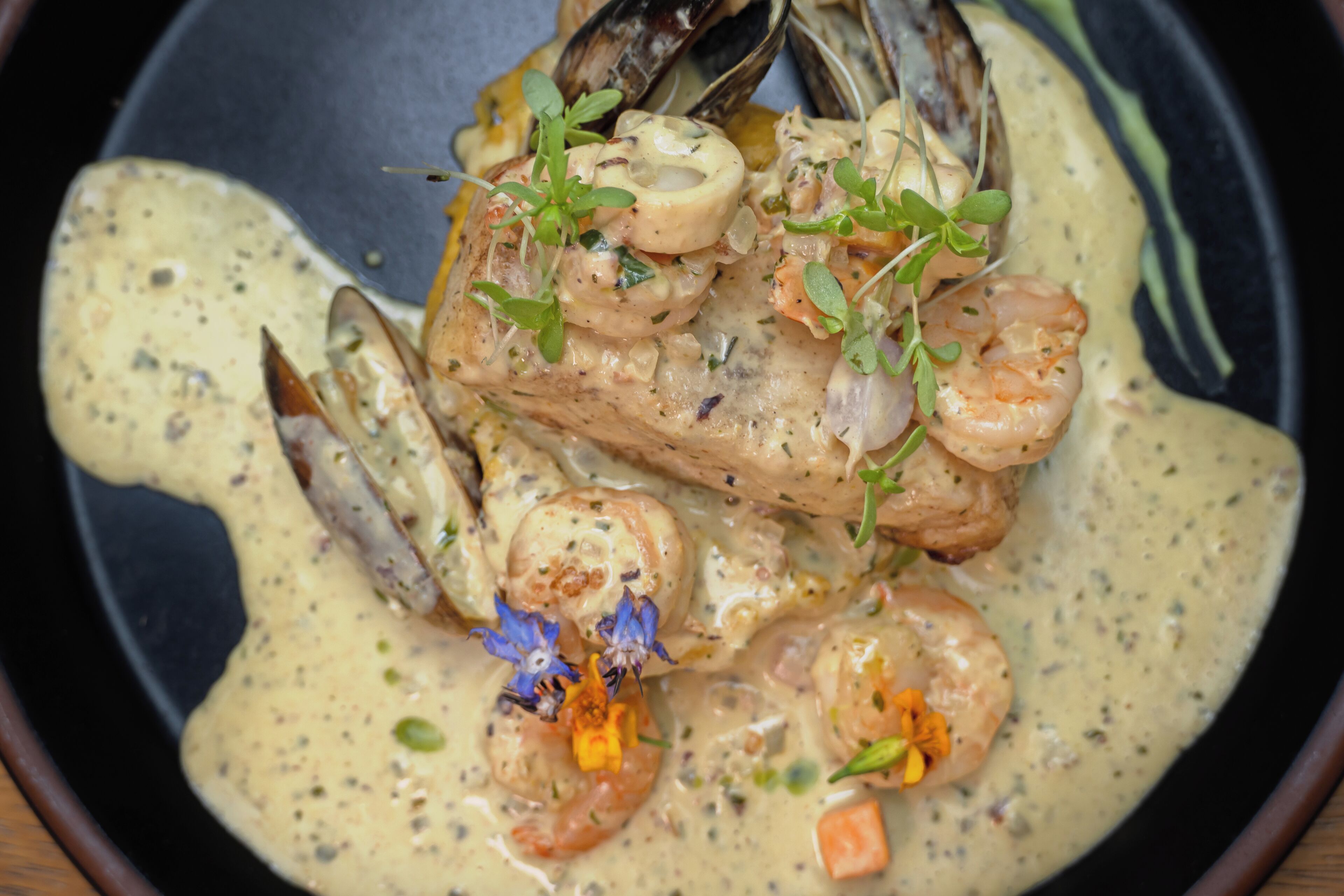 Un plato de mariscos con camarones, mejillones y hierbas en salsa cremosa, servido en un plato negro.
