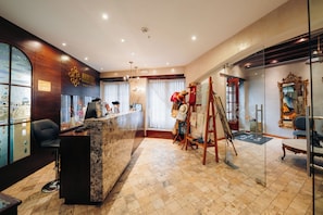 A hotel lobby with a reception desk, a large window with a view, a chandelier, and a mirror with an ornate frame.