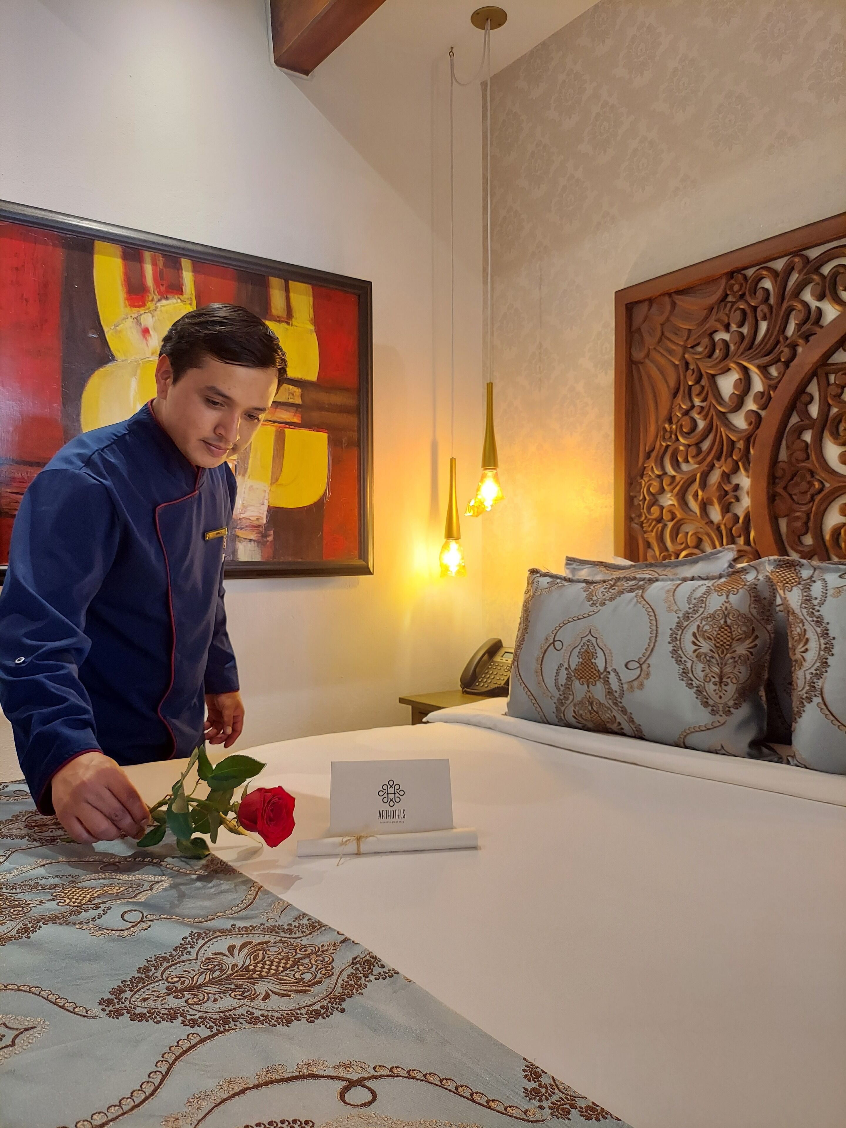 Habitación de hotel con cama, mesita de noche, teléfono, panel decorativo y un cuadro.