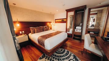 Habitación de hotel con una cama grande, mesitas de noche, un escritorio con silla, un espejo y un baño visible a través de una puerta abierta.