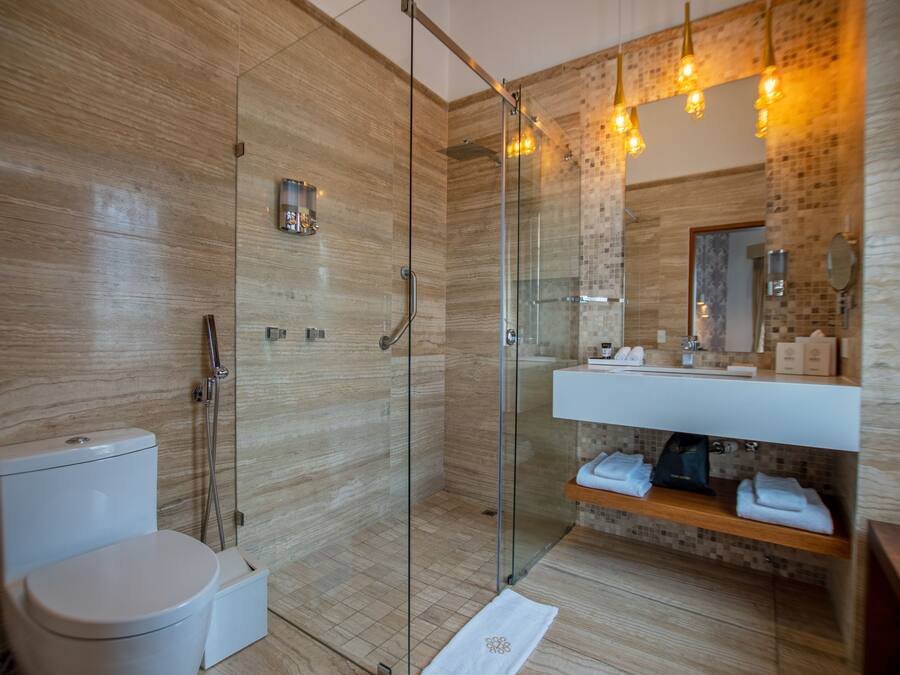 Un baño moderno con ducha de vidrio, inodoro blanco, lavabo con espejo y estante de madera con toallas.