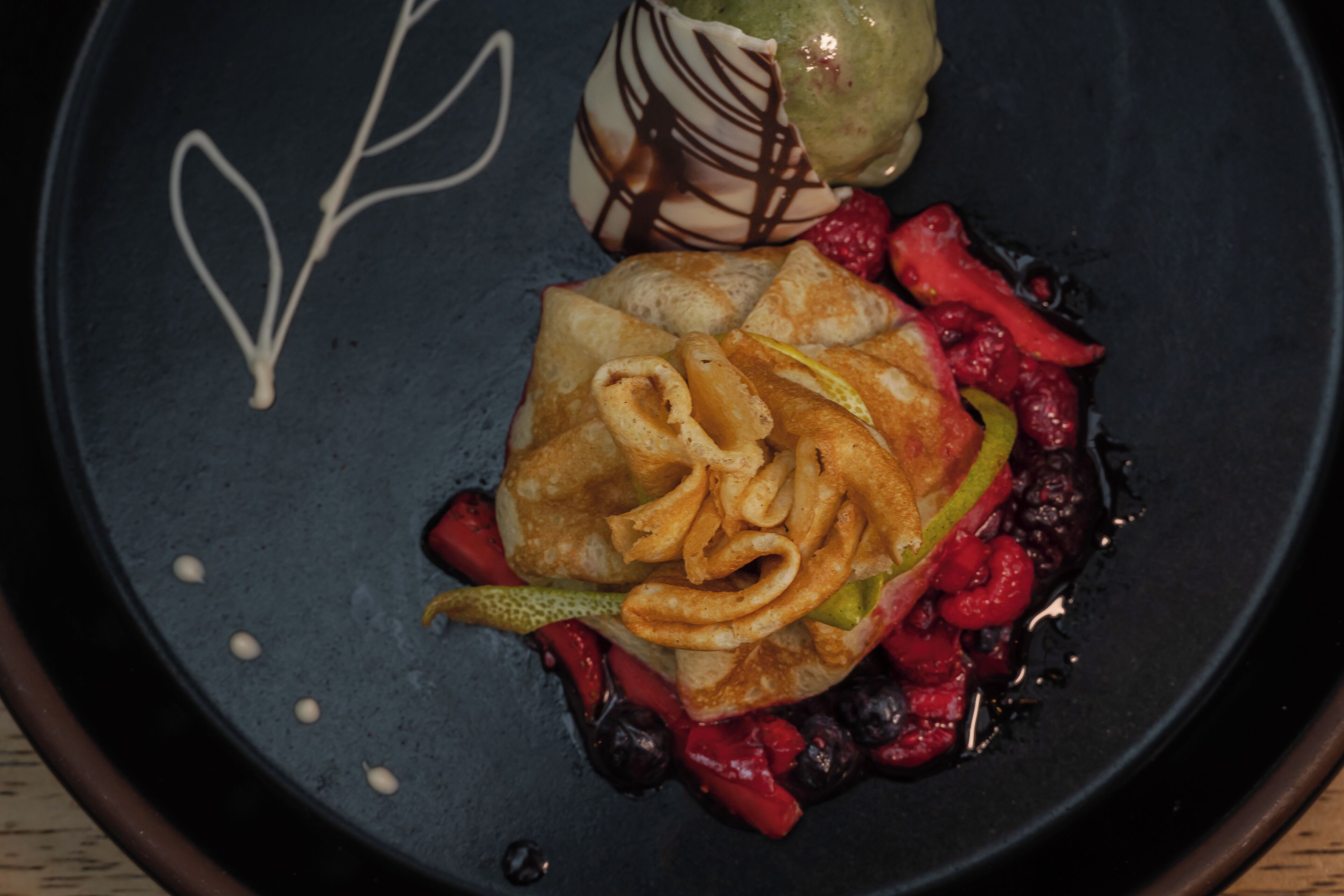 Un piattino con un dolce, frutti di bosco e un filo di cioccolato.