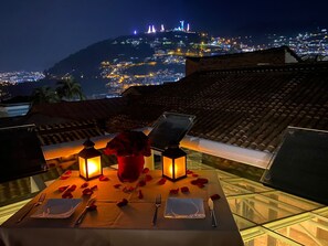 Mesa de comedor en la azotea con vista a un paisaje urbano nocturno.