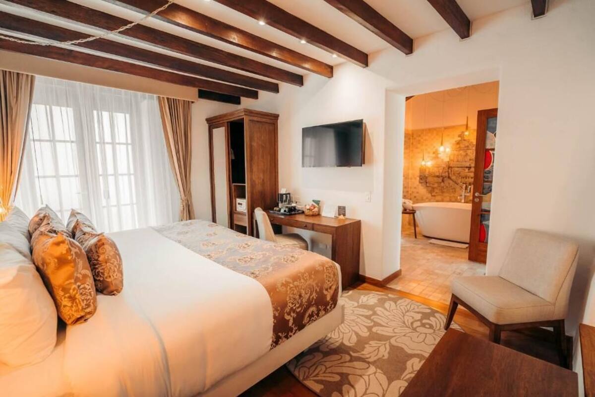 A hotel room with a large bed, a desk, a chair, and a bathroom visible through an open door.